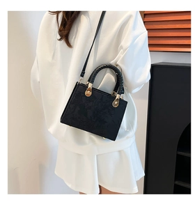 Detail of black matte crossbody bag featuring floral embossed texture and woven handles