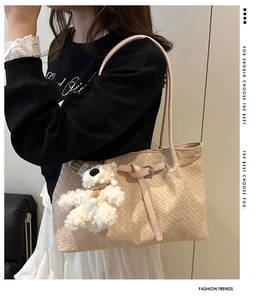 Detail view of woven leather tote bag in apricot with a plush bear charm on a model