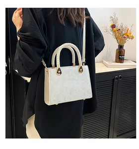 Detail of white floral embossed shoulder bag featuring woven handles and gold metal studs