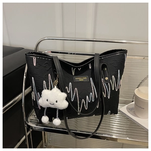 Detail of black canvas tote bag featuring wave embroidery and white cloud plush charm