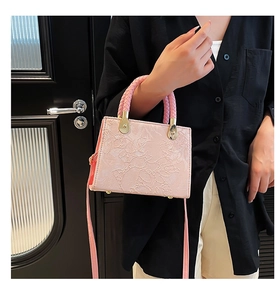 Close-up of light pink handbag featuring floral embossing and woven handles with gold hardware