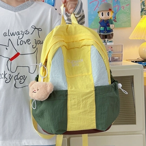 Contrast color nylon backpack with bear keychain held in a cozy indoor setting