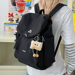 Close-up of black nylon backpack featuring a metal triangle detail and plush bear charm