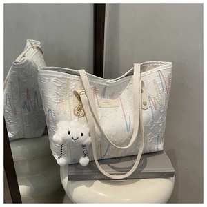 Detail of white canvas tote with wavy embroidery and fluffy cloud charm on a stand