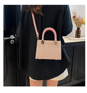 Pink embossed crossbody bag with woven handle and gold hardware in a home setting