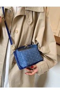 Detailansicht der blauen Denim-Tasche mit goldenen Details über einem Trenchcoat
