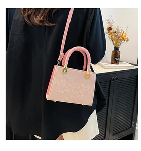 Detail of pink crossbody bag featuring floral embossing and woven handle on model