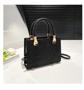 Close-up of black floral embossed handbag with woven leather handle and gold hardware detail