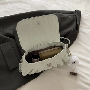 Sac bandoulière plissé vert menthe avec chaîne et porte-clés en peluche sur un costume