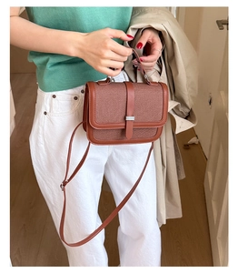 Close-up of brick red leather crossbody bag with woven texture detail and metal buckle