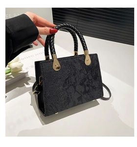 Detail of black jacquard handbag with golden hardware and cylindrical woven handle