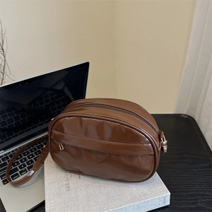 Brown vintage shell-style crossbody bag with glossy finish on a grey book background