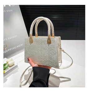 Detail of cream crossbody bag with floral embossed texture and woven handles