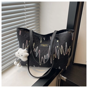 Dettaglio della borsa shopper nera con ricami colorati e ciondolo in peluche bianco