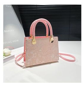 Detail of pink embossed leather handbag with woven handles and gold metal hardware