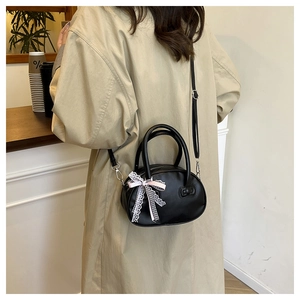 Detalle de bolso negro con lazo de encaje y correa ajustable en entorno de café