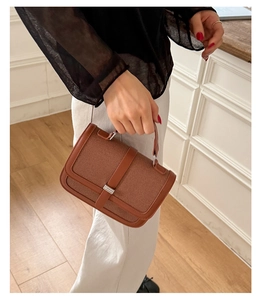 Detail of a brown woven texture handbag with leather straps and a metal buckle closure