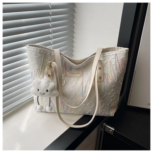 Dettaglio della borsa tote bianca con ricamo ondulato, logo in metallo e charm