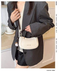 Détail du sac demi-lune blanc avec pendentif baseball porté sur un blazer gris chic
