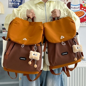 Detail of color-block nylon backpack featuring orange flap and plush mascot pendants