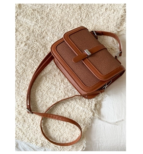 Detail of brown leather and canvas crossbody bag on a soft white plush background
