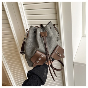 Detail of the drawstring bucket bag showing grey canvas texture and brown leather trim