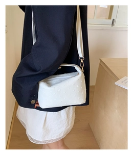 Detailed view of textured white crossbody bag featuring gold buckle and handle on model