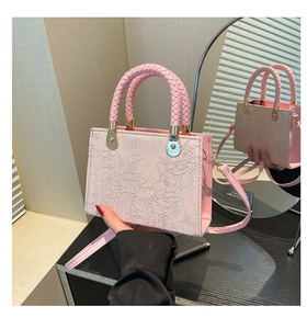 Detail of pink handbag featuring floral relief embroidery and woven top handle with gold hardware