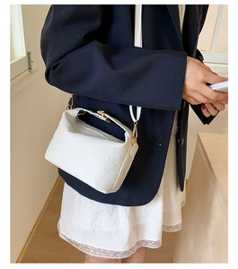 Close-up of a white ostrich texture leather mini bag with gold hardware on a blue suit model
