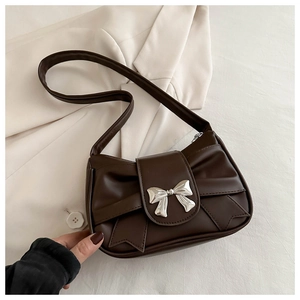 Detailed view of dark brown shoulder bag with metallic silver bow buckle on beige blazer