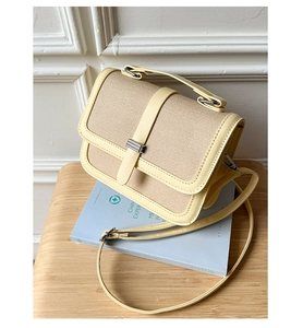 Detail of a light yellow woven crossbody bag with faux leather trim on a blue book