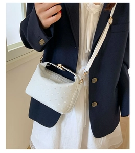 Close-up of white crossbody bag with ostrich texture and gold hardware on model
