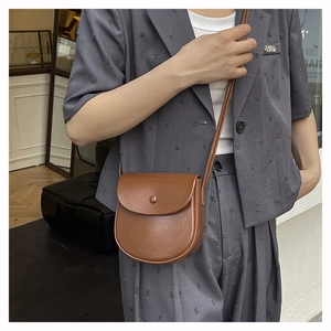 Side view of a vintage dark brown leather saddle bag styled on a grey suit model