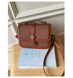 Vintage brown crossbody bag with woven texture and silver metal bar on a wooden stool