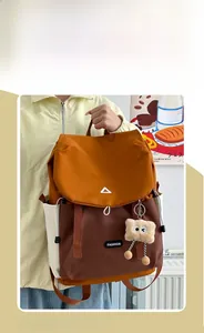 Detail of color-block nylon backpack featuring orange, brown, and cream panels with monster charm