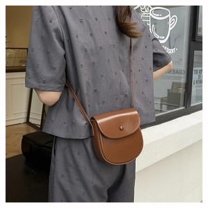 Close-up of brown glossy leather saddle bag with round buckle shown on a model