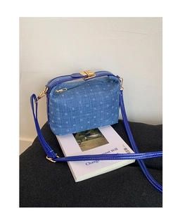 Detail of blue denim shoulder bag with pattern texture and gold metal buckle on white book