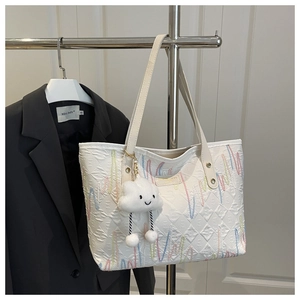 Detail view of white quilted tote bag featuring colorful embroidery and cloud pendant