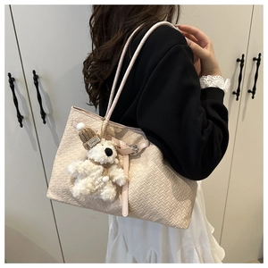 Detail of beige woven tote bag with circular straps and a plush bear charm on white background