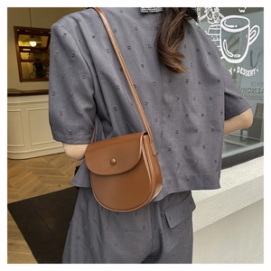 Brown leather saddle bag shown on a grey outfit in a modern urban shop setting