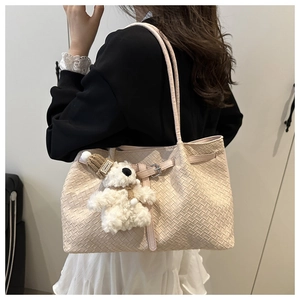 Detail view of a beige woven tote bag featuring a cute teddy bear charm and sleek strap
