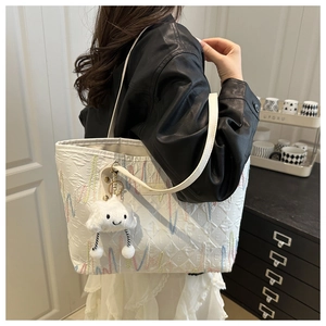 Close-up of a white quilted tote bag with wave embroidery and cloud charm on a model