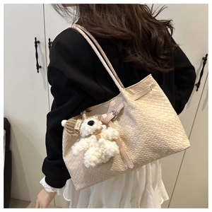 Detail of beige woven tote bag featuring a cute white plush bear charm and long strap