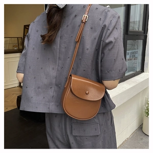 Close-up of a brown leather saddle bag on model showing fine texture and adjustable strap
