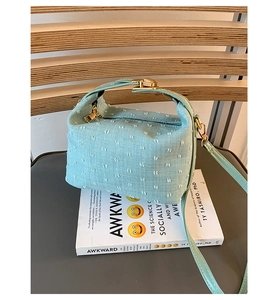 Detail der mintgrünen Stoffhandtasche mit goldener Hardware auf einem Holzstuhl