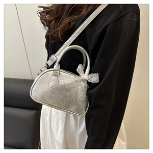 Dettaglio borsa a bauletto argento con graffiti, fiocco in pizzo bianco e tracolla