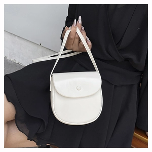 Detailed view of white saddle crossbody bag with flap and decorative button on black dress