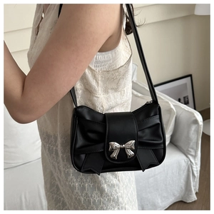 Detail of a black pleated shoulder bag featuring a silver metal bow clasp on white lace dress
