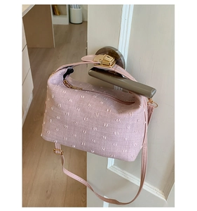 Close-up of pink textured crossbody bag with floral fringe detail and golden buckle