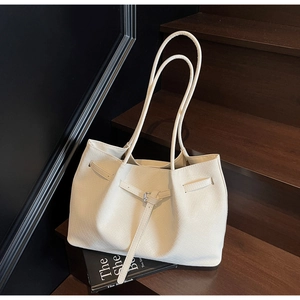 Détail du sac cabas tissé crème avec boucle décorative et grande capacité sur un escalier
